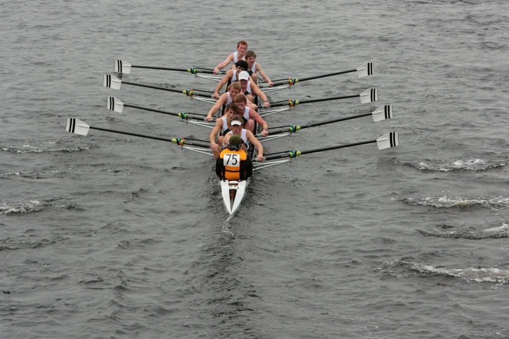 A team of rowers in a boat, with oars extended, competing on a body of water.